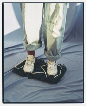 Person stands on grass mat while wearing white sneakers