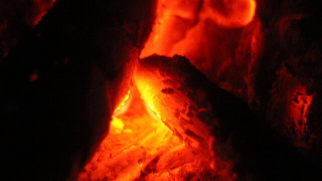 Close up of burning wood logs blazing in flames inside black wrought iron wood burning fire.