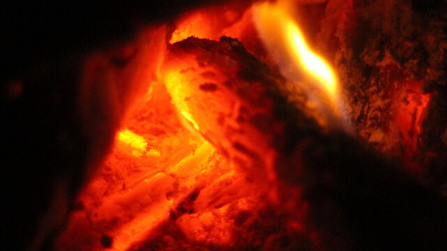 Close up of burning wood logs blazing in flames inside black wrought iron wood burning fire.