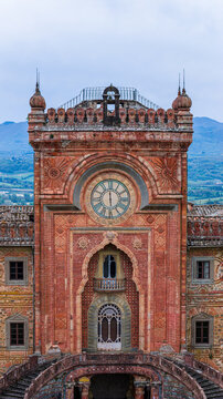 Aerial view of the intricate Moorish facade of Sammezzano Castle featuring a large clock and ornate terracotta details against a backdrop of rolling hills in Reggello, Tuscany, Italy.