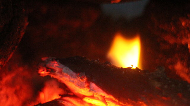 Close up of burning wood logs blazing in flames inside black wrought iron wood burning fire.