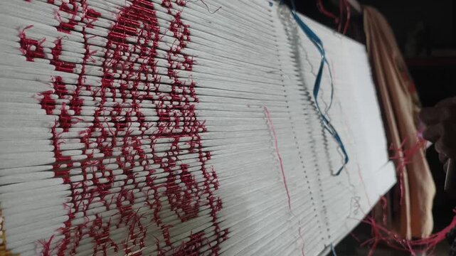 Close-up of artisan hands meticulously tying bundles of threads with plastic/raffia to create intricate patterns for traditional ikat weaving