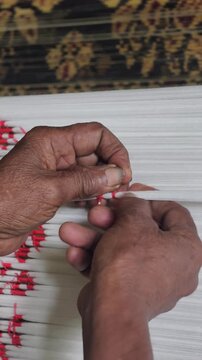 Close-up of artisan hands meticulously tying bundles of threads with plastic/raffia to create intricate patterns for traditional ikat weaving