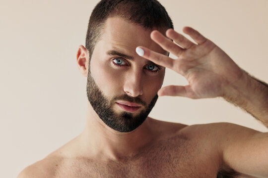 Man Shields Eyes From Light While Posing Against a Plain Background