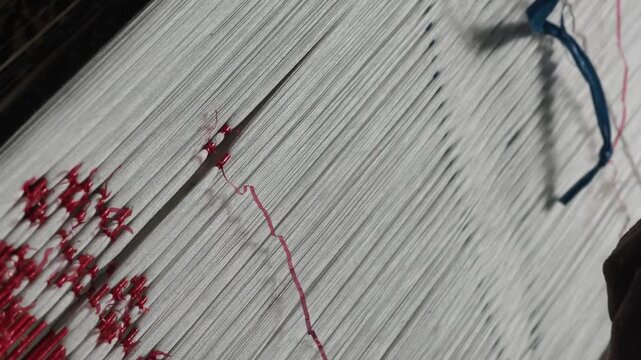 Close-up of artisan hands meticulously tying bundles of threads with plastic/raffia to create intricate patterns for traditional ikat weaving