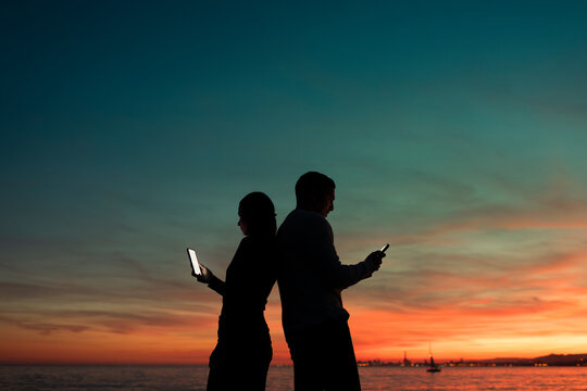 Amused couple using phones at striking sunset