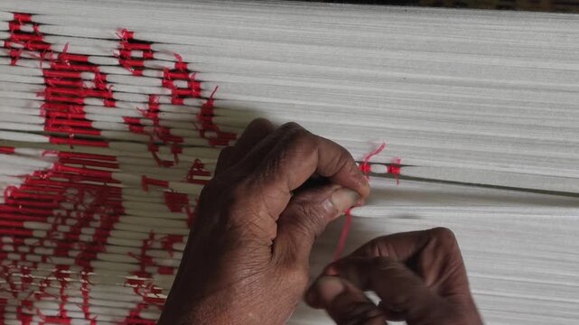 Close-up of artisan hands meticulously tying bundles of threads with plastic/raffia to create intricate patterns for traditional ikat weaving
