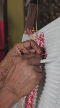 Close-up of artisan hands meticulously tying bundles of threads with plastic/raffia to create intricate patterns for traditional ikat weaving