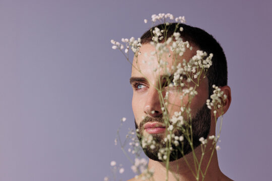 Man With Beard Stands Among White Flowers Against a Purple Backdrop