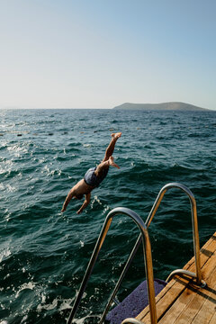 Young man diving into the blue Mediterranean Sea from a deck