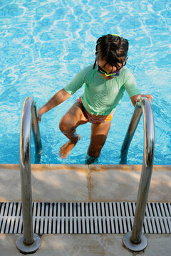 Little girl wearing swimming goggles climbing up the pool ladder