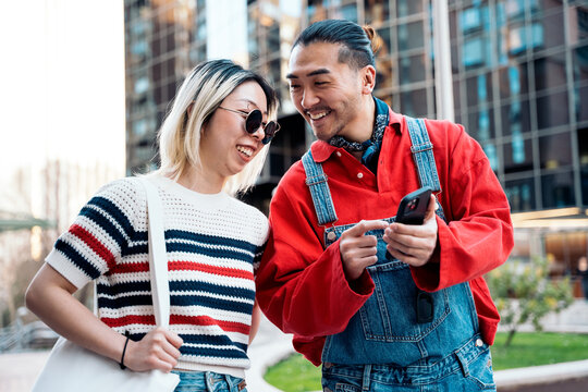 Happy asian couple smiling using smartphone outdoors
