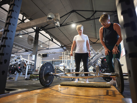 Personal Trainer assisting client with weight lifting equipment at gym