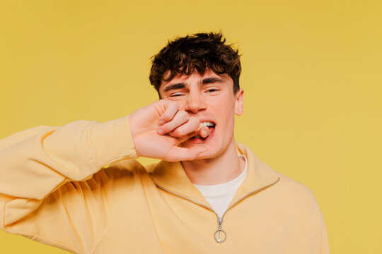 Man biting finger looking at camera against yellow wall