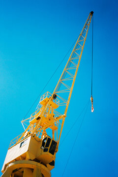 Yellow port crane with hook against blue sky 