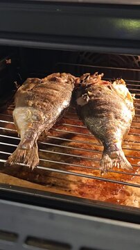Two whole grilled sea bream fish laying on an oven wire rack, perfectly roasted until golden brown, prepared for a healthy Mediterranean seafood dinner.