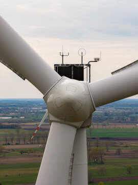 Aerial view of the hub and blades of a large wind turbine overlooking rural fields and farmland in Debsk, Masovian Voivodeship, Poland.