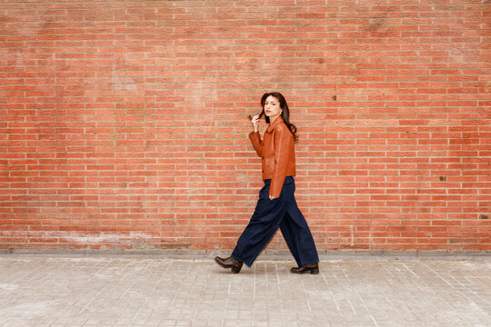 Woman Walks on Sidewalk Near Red Brick Wall