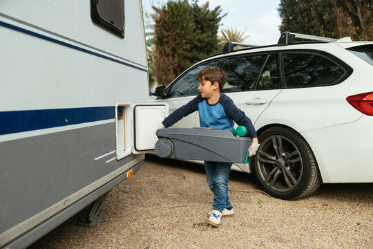 Boy wearing gloves pulling portable toilet tank from a caravan