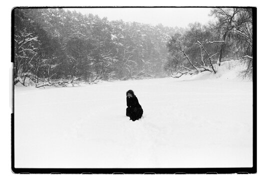 Film B&W Photo of a Woman Kneeling Alone in Vast Snowy Field