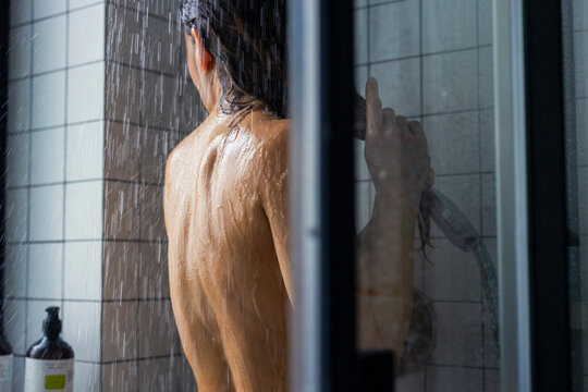 Woman Showering In Modern Tiled Bathroom