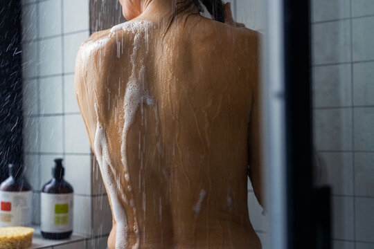 Woman Showering In Tiled Bathroom With Soapy Back