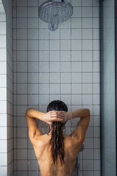 Woman Showering Under Rain Showerhead In Tiled Bathroom