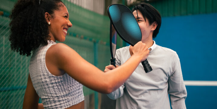 Diverse couple having fun with pickleball paddles on an indoor court