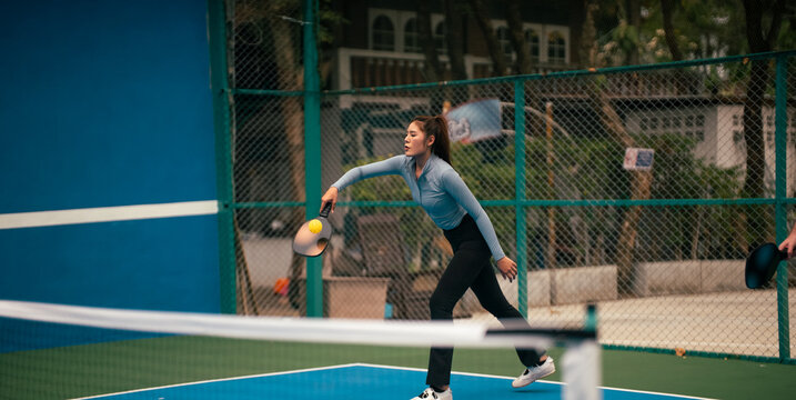 Young woman playing pickleball on court, hitting ball with technique