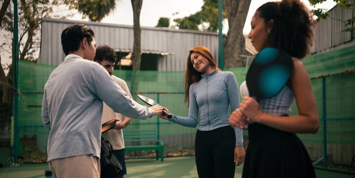 Instructor handing pickleball paddle to new player on outdoor court