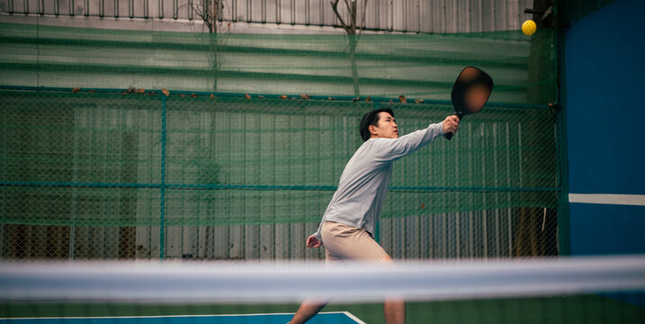 Young man striking pickleball on court developing active lifestyle