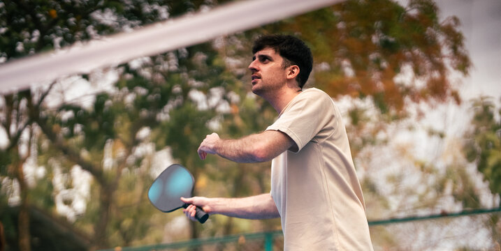 Young man holding a paddle while playing pickleball on outdoor court