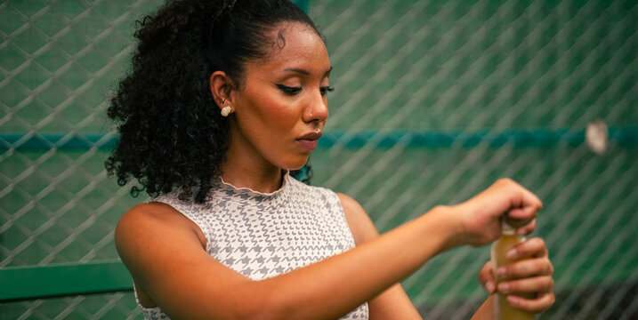 Woman opening bottle, hydrating during exercise break on a court