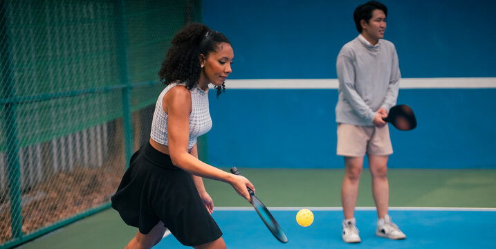 Woman playing pickleball and hitting a yellow ball on blue court