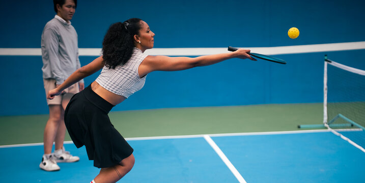Woman hitting pickleball ball during exciting game on blue court