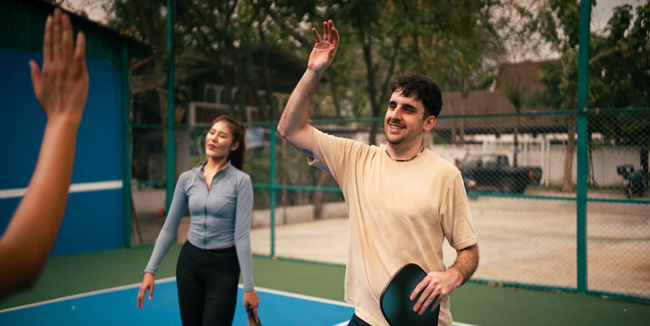 People playing pickleball on court, smiling and giving a high five