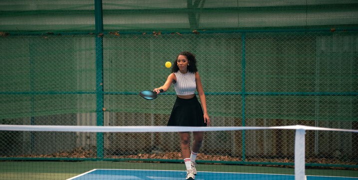 Woman playing pickleball on court, hitting yellow ball with paddle