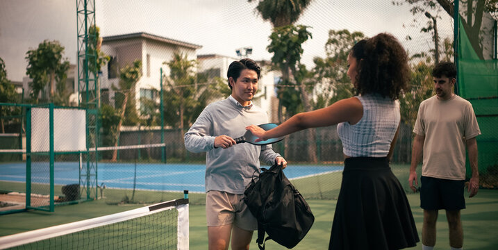Friends preparing for pickleball game on outdoor court holding racket