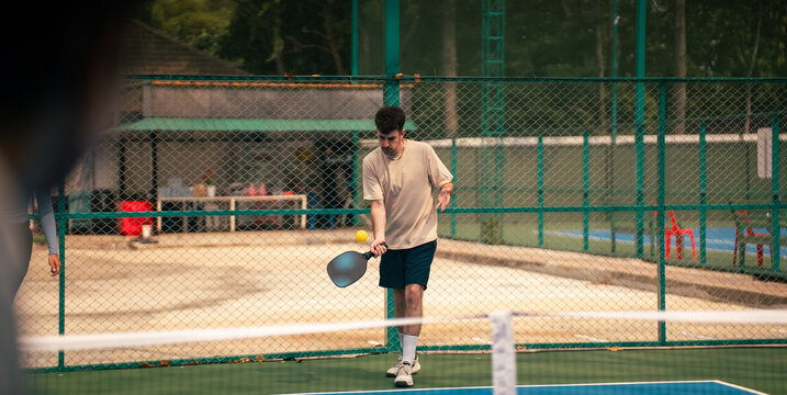 Young man playing pickleball on outdoor court hitting yellow ball