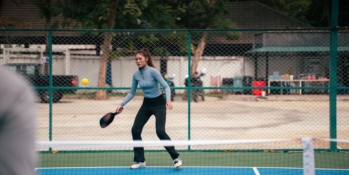 Young woman playing pickleball outdoors, hitting ball with paddle