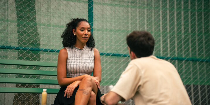 Woman and man having deep conversation outdoors on green sport court