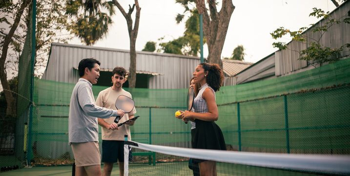 Diverse friends preparing for pickleball game, learning on court