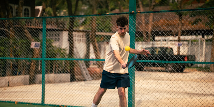 Young man playing pickleball on an outdoor court, hitting the ball