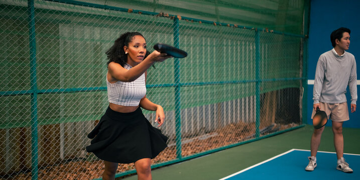 Woman playing pickleball on court, focusing on ball with man partner