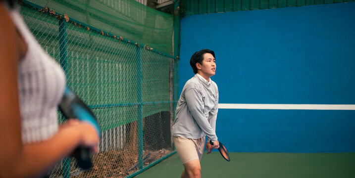 Young asian man playing pickleball on indoor court, ready for action