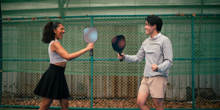 Diverse couple holding paddles on court, celebrating points together