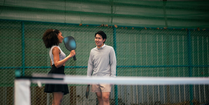 Diverse couple enjoying pickleball game, communicating and smiling