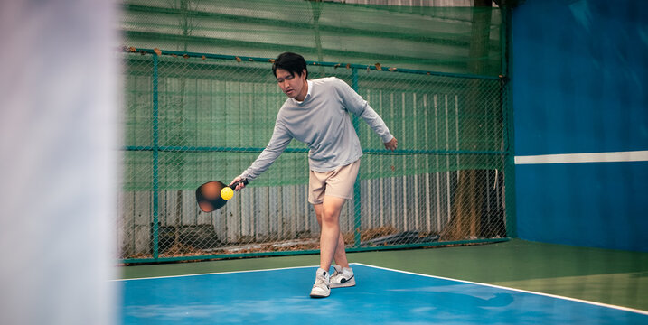 Young man playing pickleball, focusing on hitting ball during game