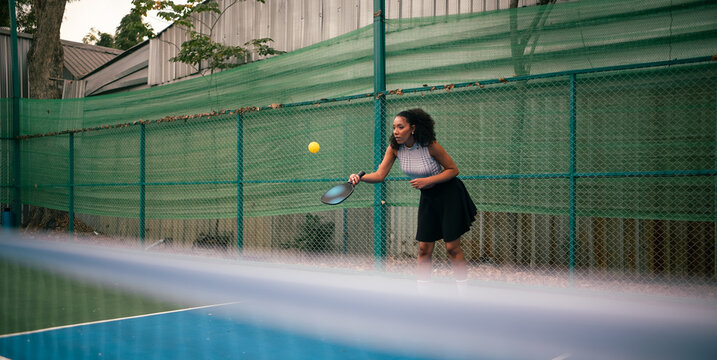 Woman playing pickleball on court, hitting ball with specific paddle