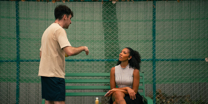 Coach teaching pickleball basics to a focused woman on court bench